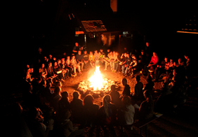Viele Menschen sitzen im Kreis um ein Lagerfeuer in der Nacht
